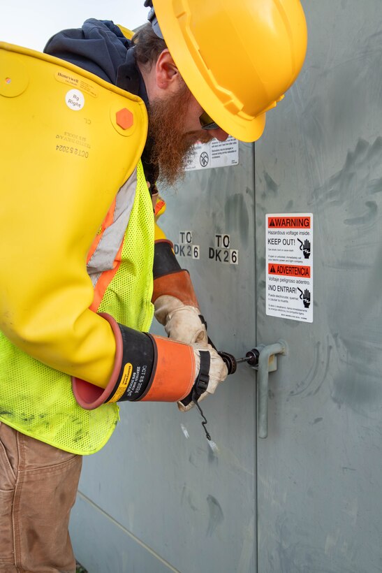 Man in hard hat and protective equipment unlocking an electrical box.
