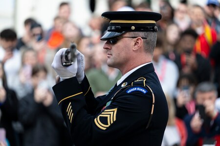 A U.S. Army Soldier dressed in ceremonial dress uniform is holding a rifle horizontally in both hands while inspecting it during a changing of the guard ceremony at the Tomb of the Unknown Soldier.