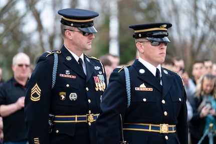 A U.S. Army Soldier in dark blue ceremonial dress uniform is standing behind another Soldier while inspecting his uniform at the Tomb of the Unknown Soldier during the changing of the guard ceremony.