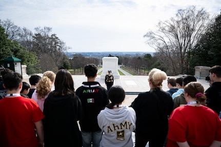 A large crowd (foreground) is watching a U.S. Army Soldier in dark blue ceremonial dress uniform at the Tomb of the Unknown Soldier.
