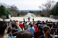 A large crowd (foreground) is watching three US Army Soldiers in dark blue ceremonial dress uniforms perform a changing of the guard ceremony at the Tomb of the Unknown Soldier.
