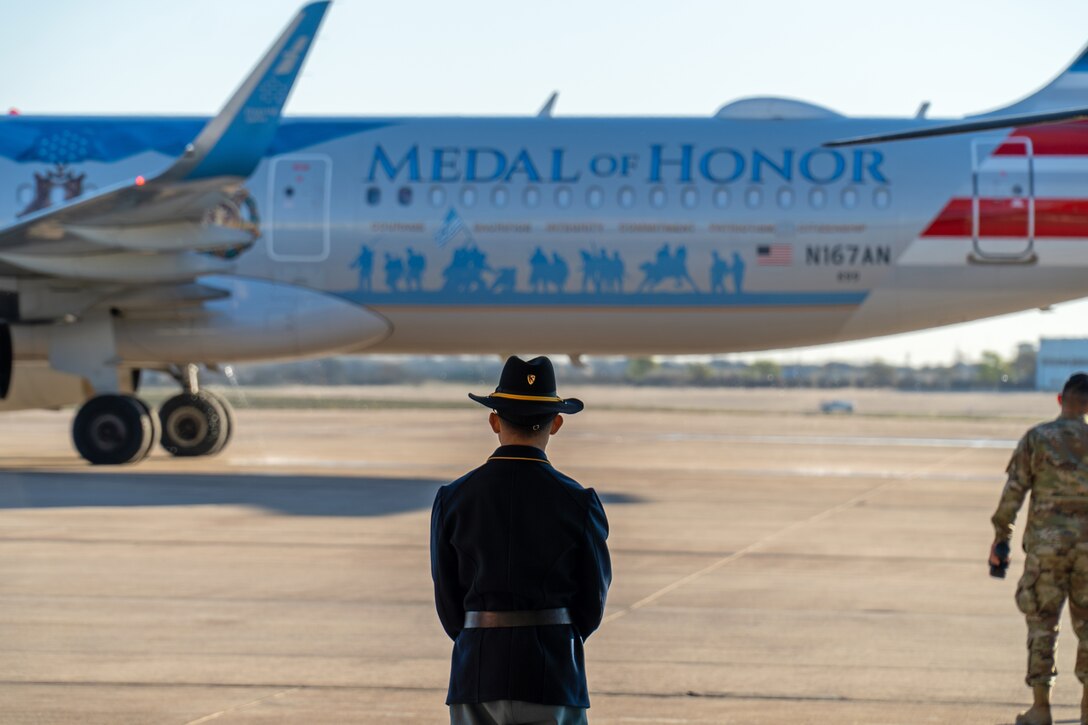 A soldier stands on a runway facing a plane that says "Medal of Honor" on the side.