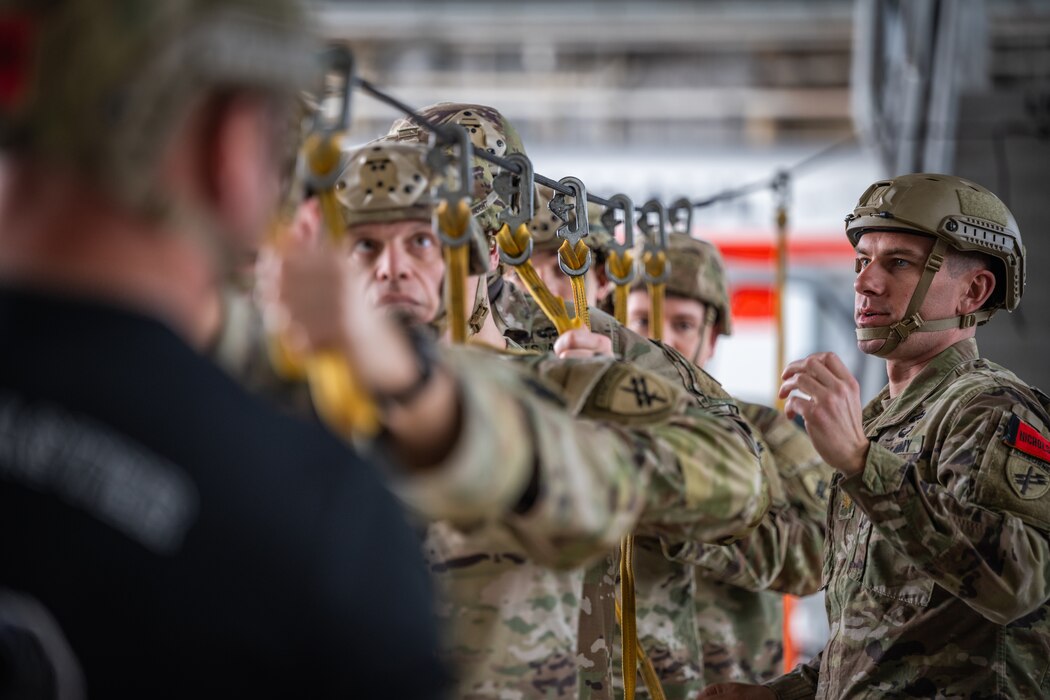 Army soldiers in military uniform stand single file with a yellow cord clipped onto a dark cable above their heads