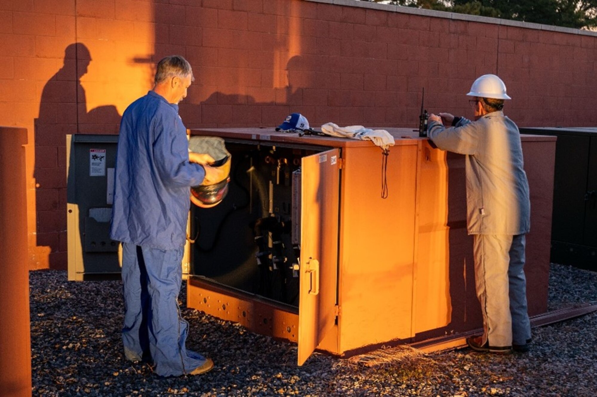 Man puts on helmet next to power box and another man uses a communication device. (U.S. Air Force photo by Airman 1st Class Donnell Ramsey)