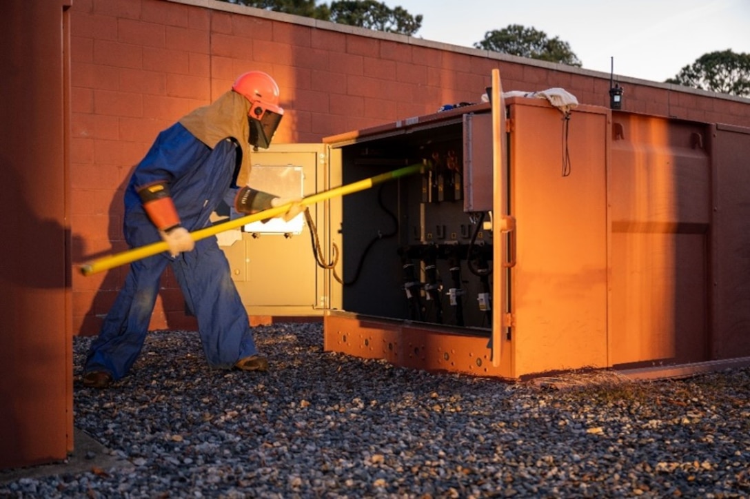 Man turns on power box with a stick. (U.S. Air Force photo by Airman 1st Class Donnell Ramsey)