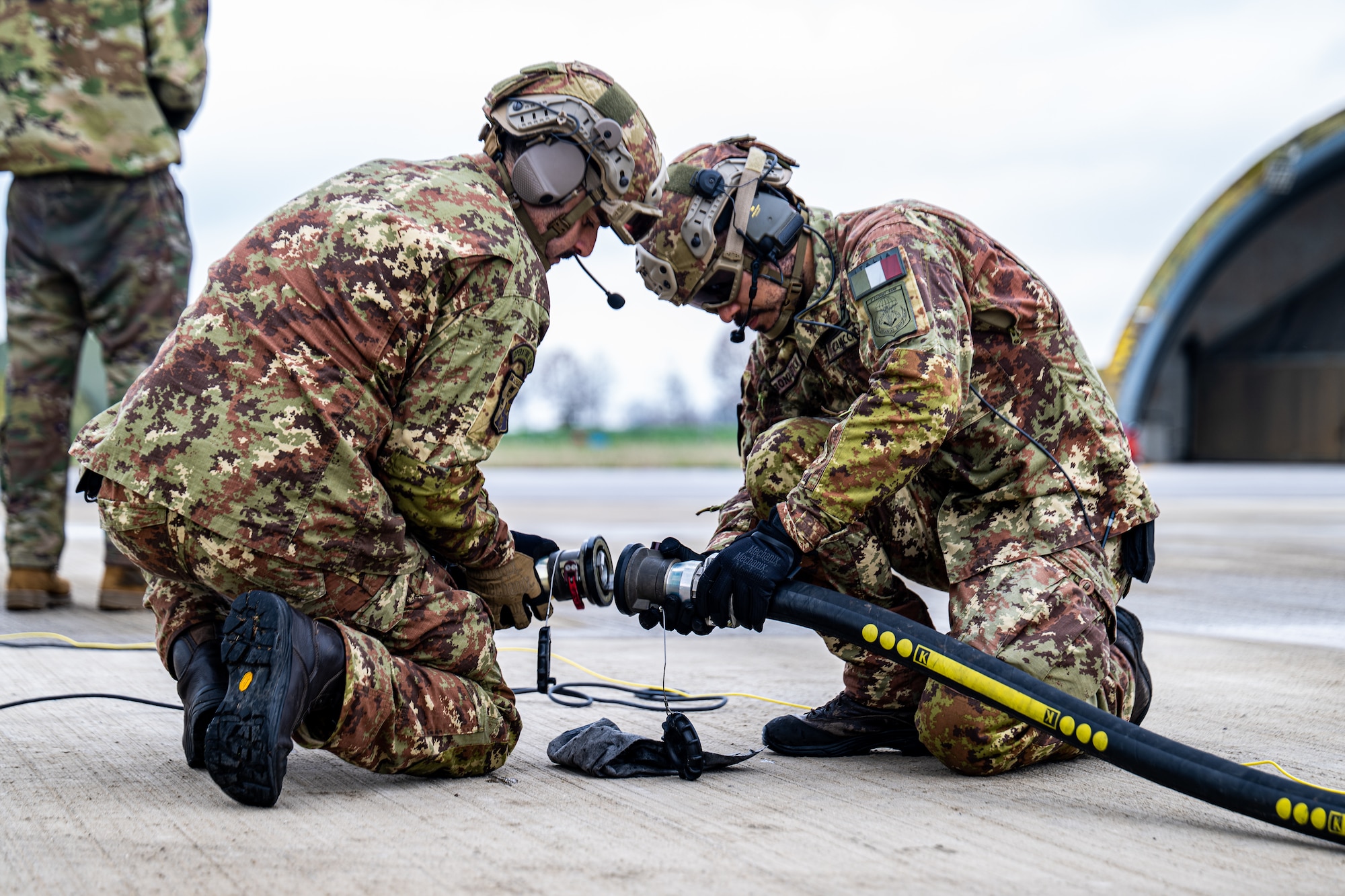 Italian air force Airmen work together to attach a fuel hose together for a hot-pit during Exercise Fighting Wyvern 25-01 at Istrana Air Base.