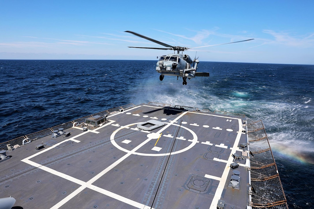 A helicopter prepares to land aboard a ship at sea.