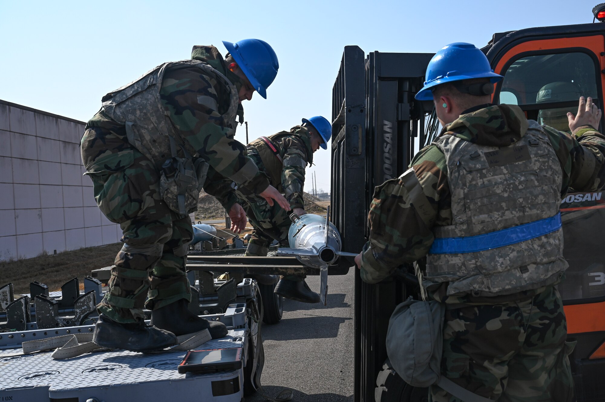 U.S. Air Force Staff Sgt. Candice Croes, left, 8th Maintenance Squadron conventional maintenance support craftsman, Senior Airman Jonathan Bowe, center, 8th MXS munitions inspector, and Staff Sgt. Alec Linn, 8th MXS conventional maintenance crew chief, transport a training munition onto a loader during Freedom Shield 25 at Kunsan Air Base, Republic of Korea.
