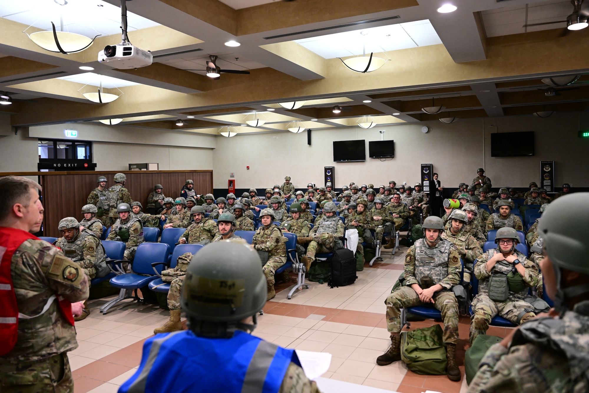 U.S. Air Force Airmen sit in a large room to be briefed.