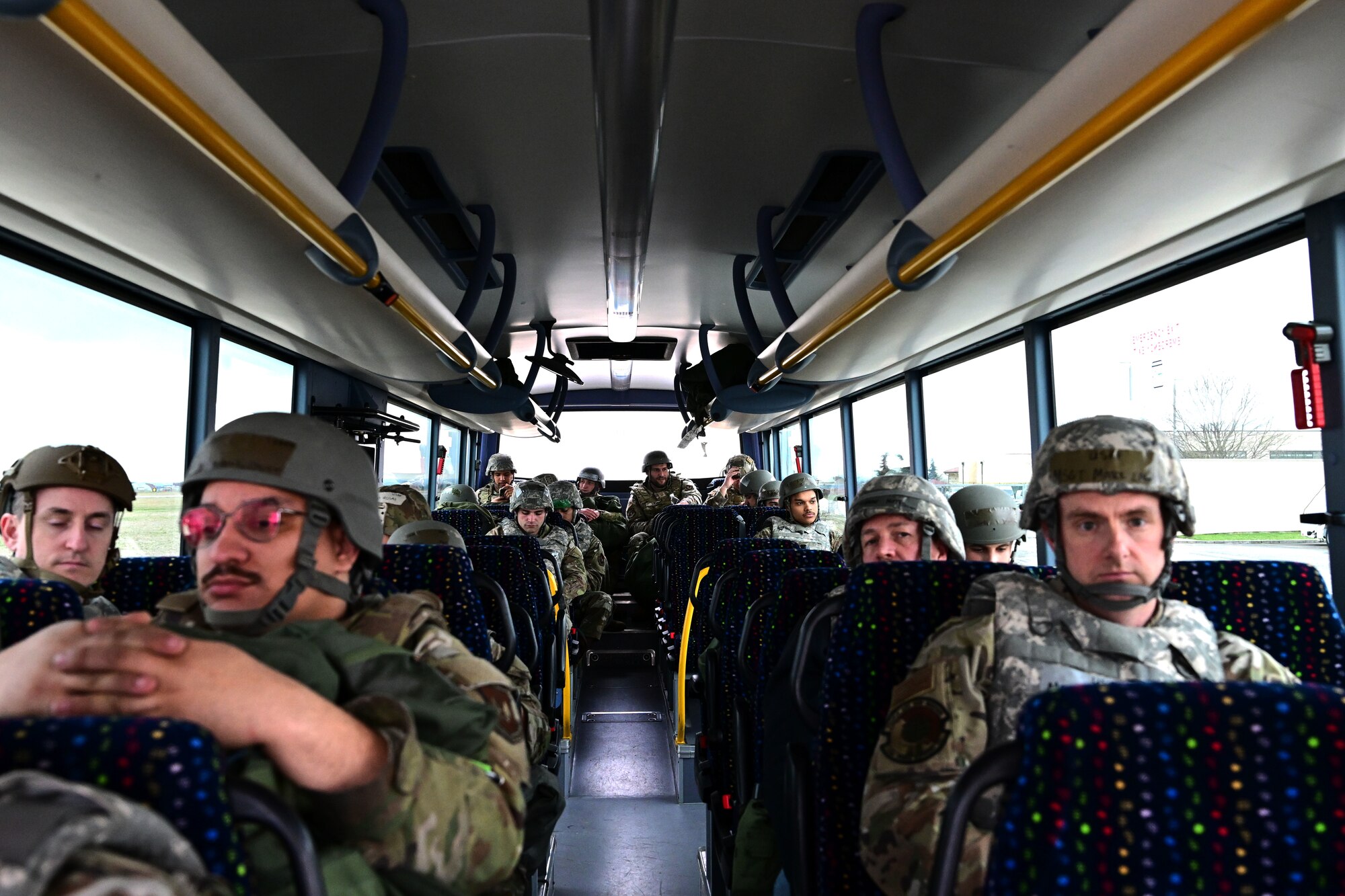 Service members wearing chemical gear sit on a bus