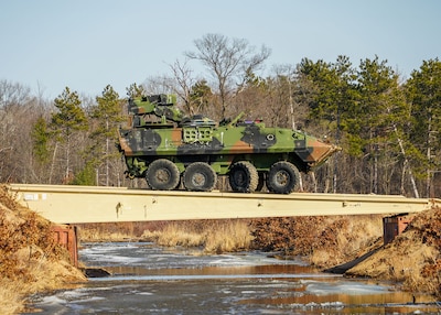 An MRAP sits on a bridge span over a narrow stream of water