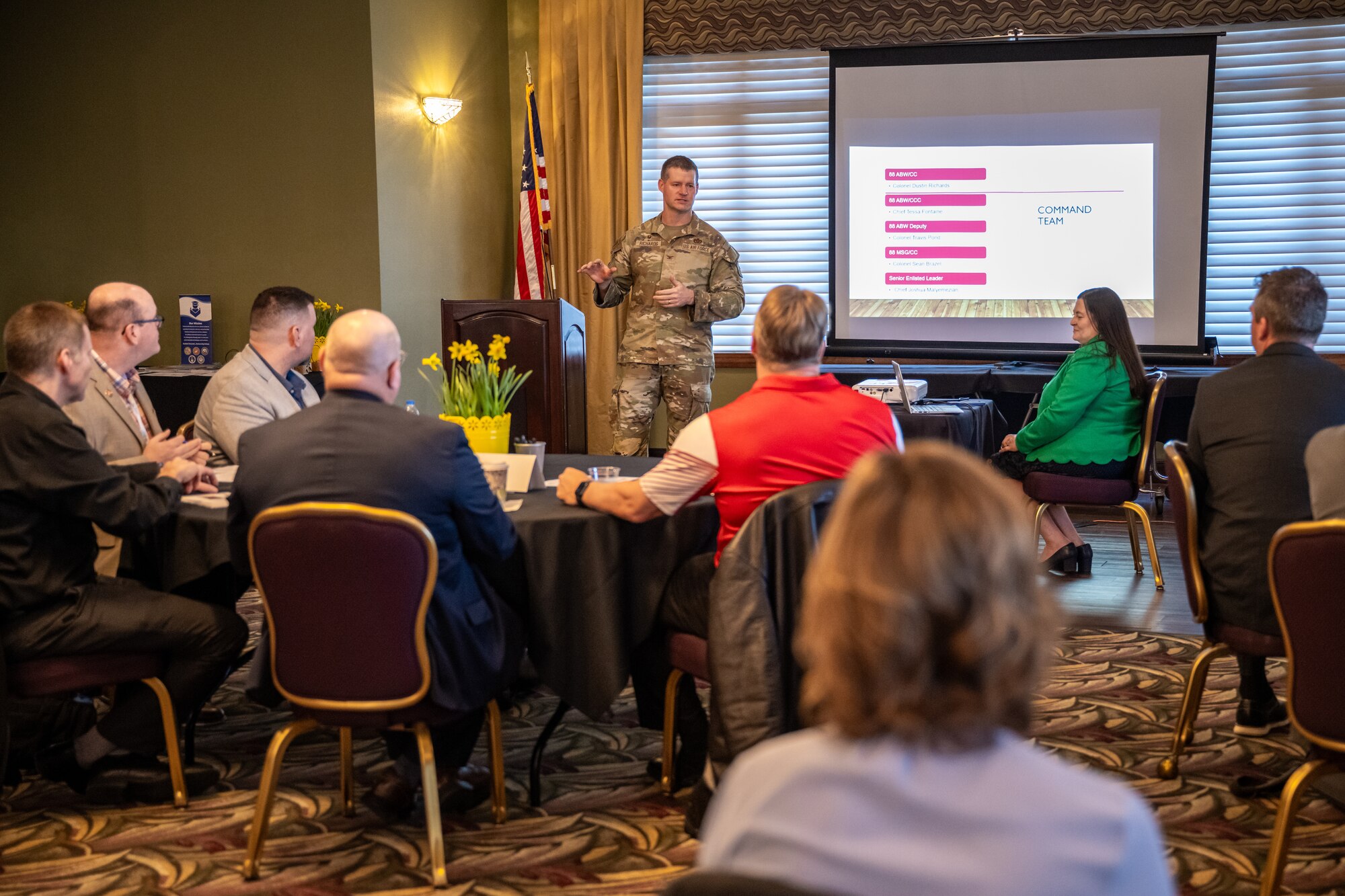 Col. Richards, in military uniform, stands in front of a room full of people giving a speech
