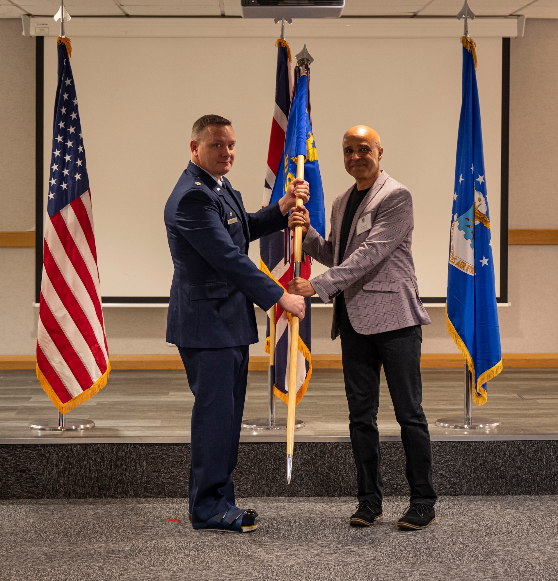 U.S. Air Force Lt. Col. Brian Slater, left, 100th Security Forces Squadron commander, presents a guidon to Lou Handy, Mildenhall Cricket Club chairman, during the honorary commanders’ induction ceremony at RAF Mildenhall, England, March 21, 2025.