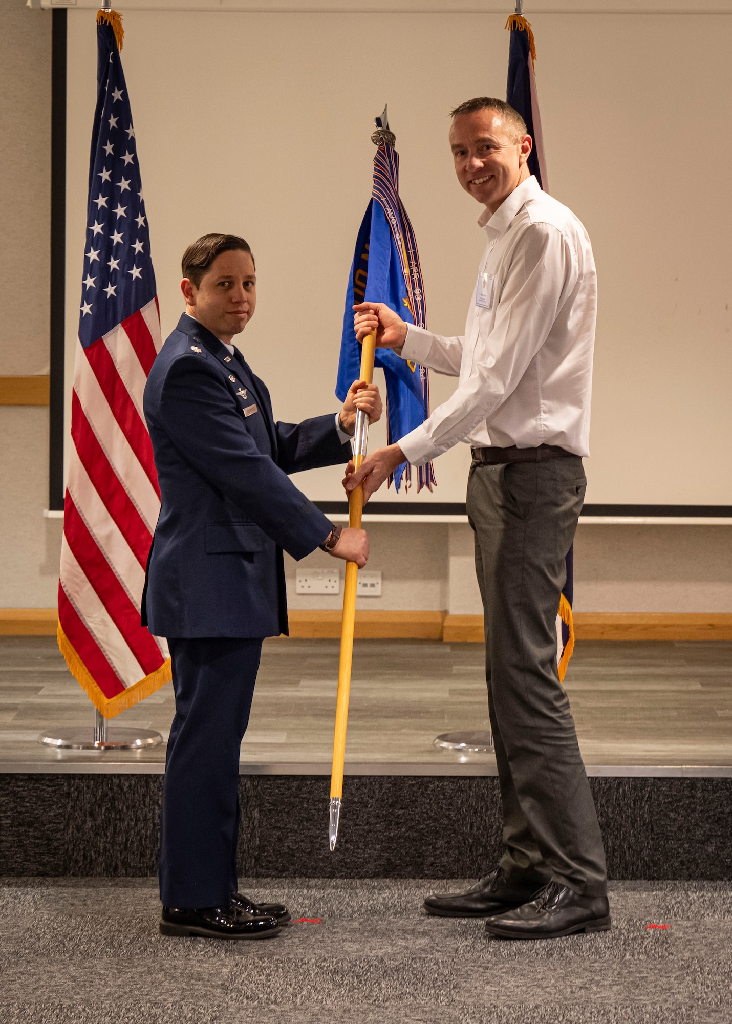 U.S. Air Force Lt. Col. Emilio Rodriguez, left, 100th Maintenance Squadron commander, presents a guidon to Michael Nelson, West Suffolk College head of engineering, during the honorary commanders’ induction ceremony at RAF Mildenhall, England, March 21, 2025.