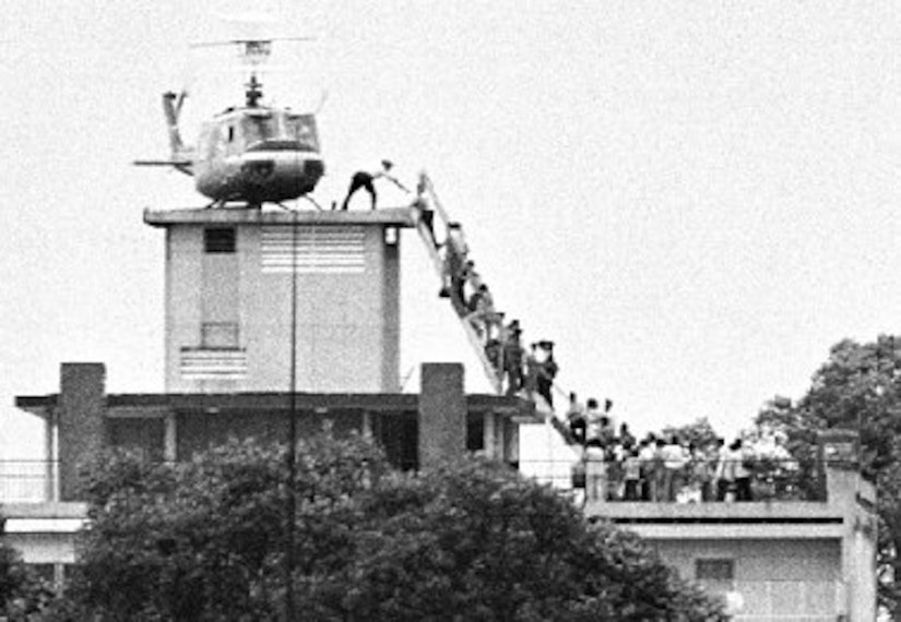 People climb up a ladder to a helicopter on a roof.