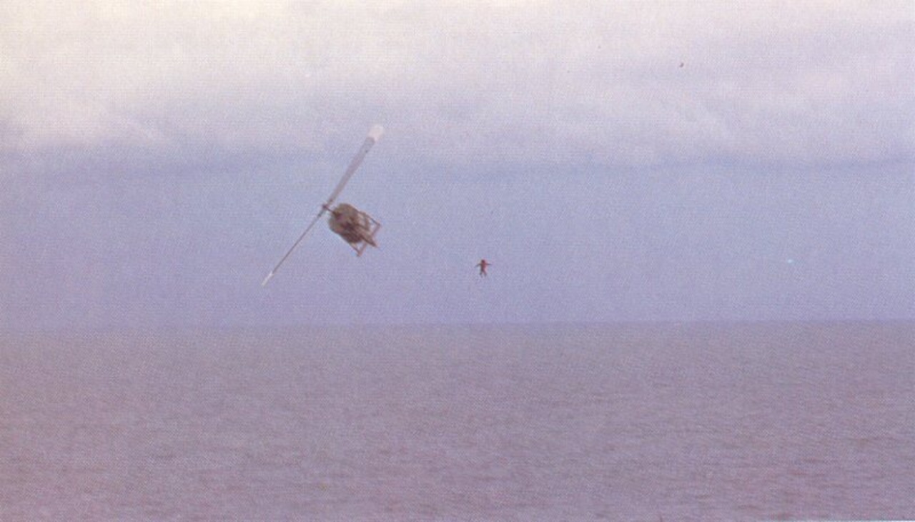 A helicopter banks to the left as a man falls into the water.