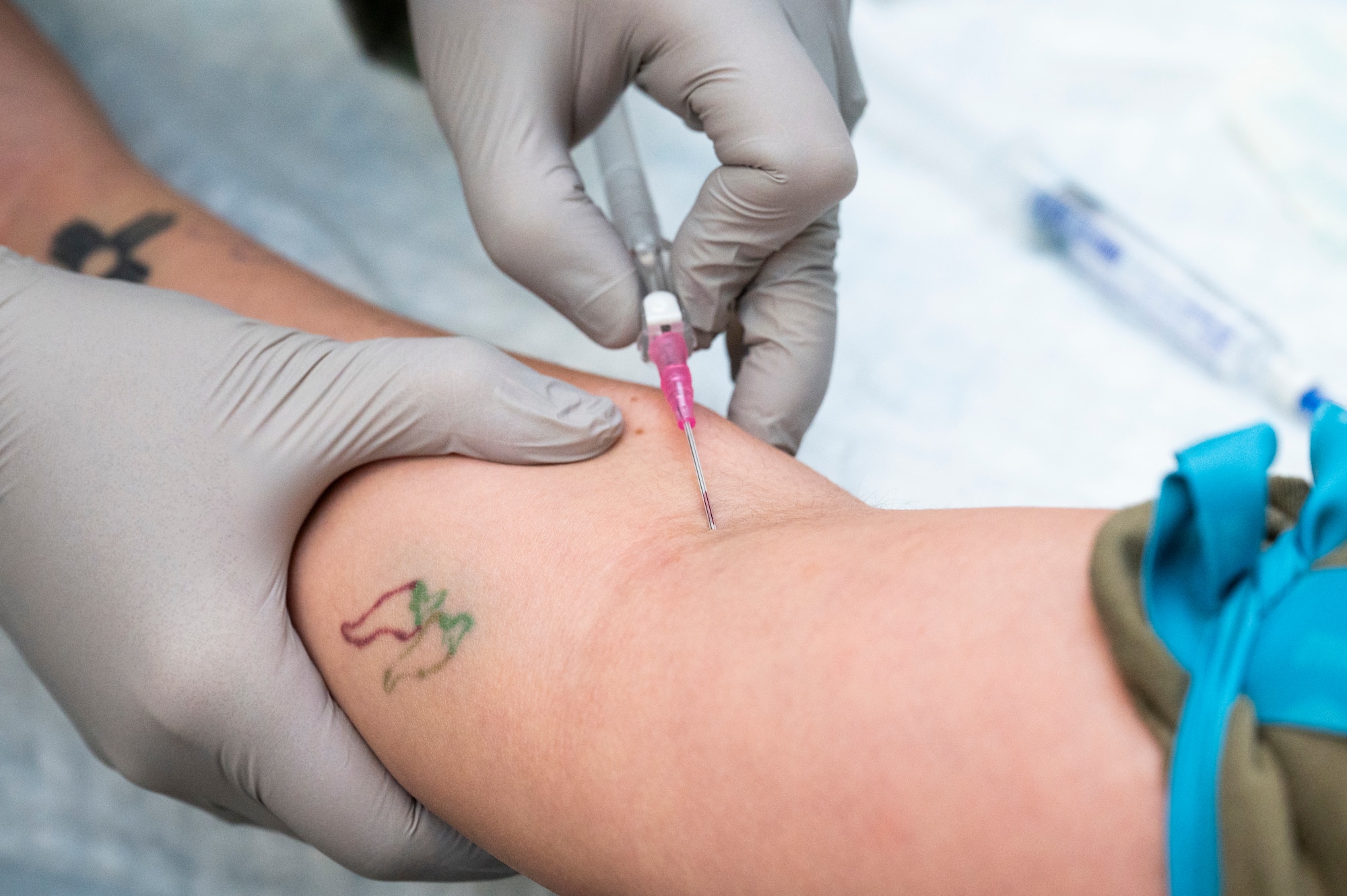 A 5th Medical Group Airman sticks a needle into another Airman's arm for IV training.