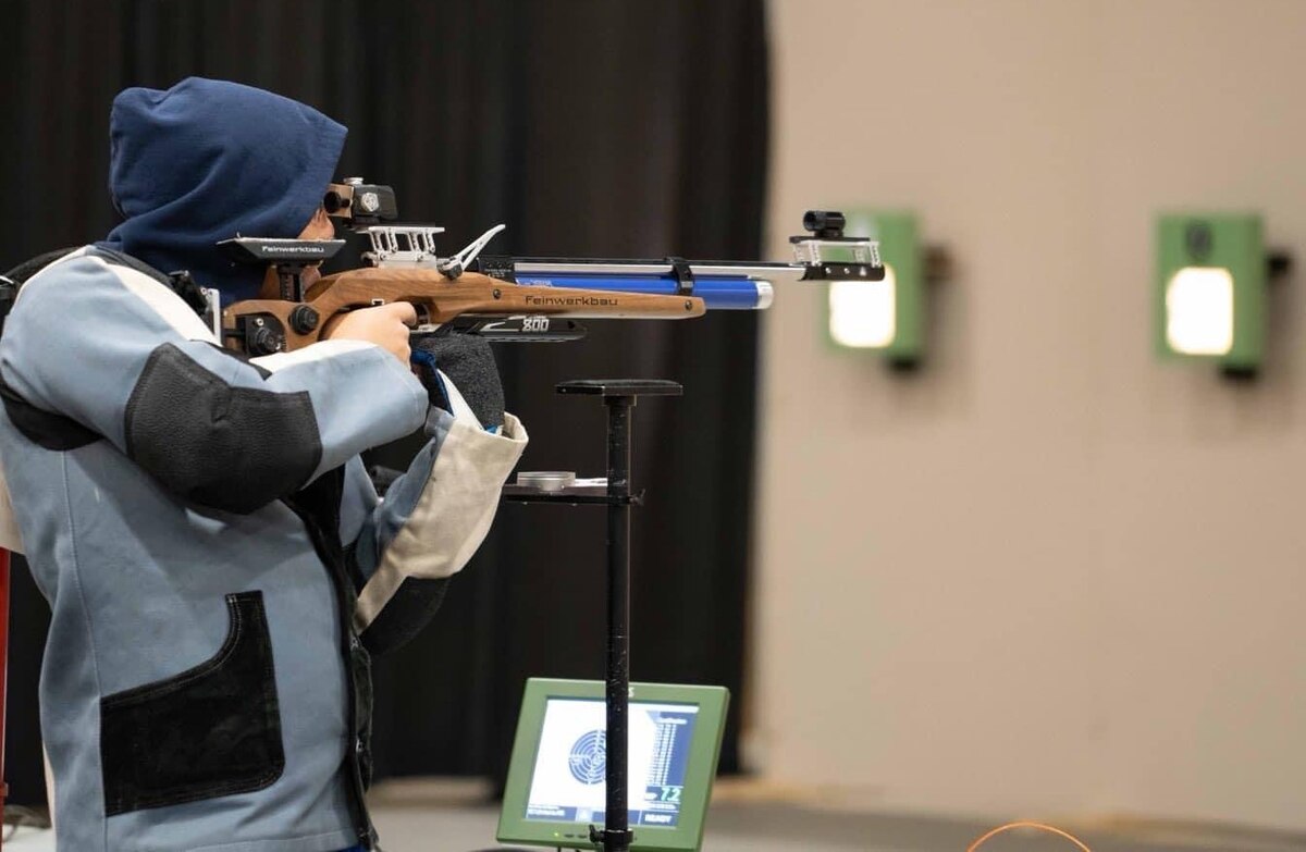 side view of Lin taking aim at a target with an air rifle.