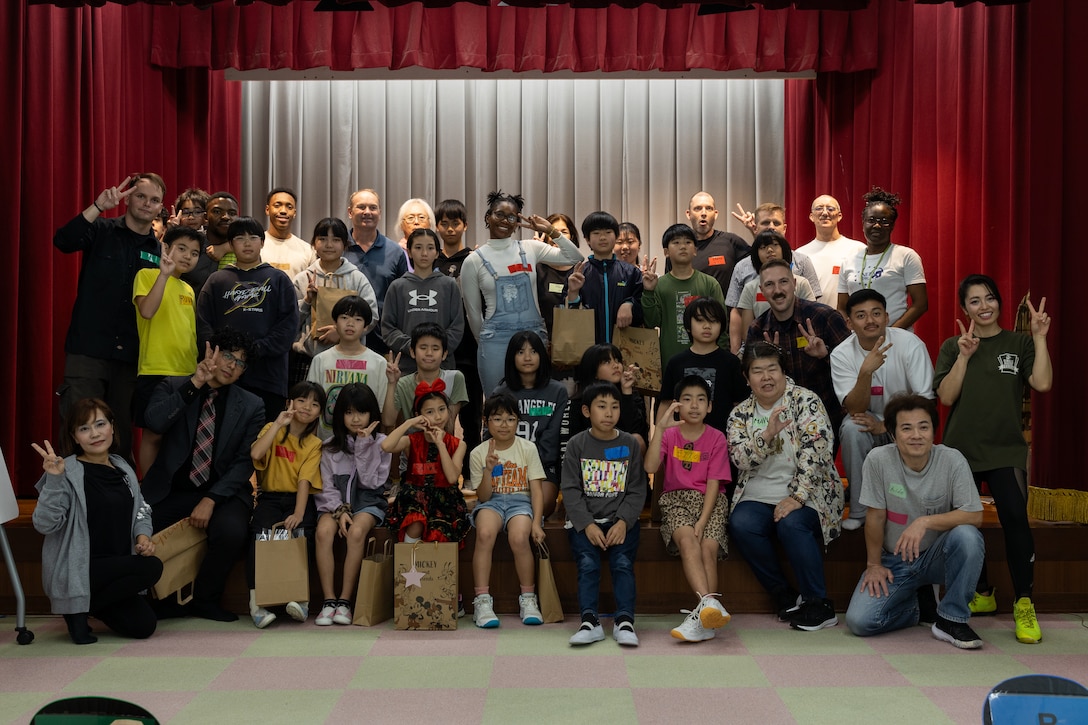 U.S. Marine volunteers, local elementary students, and members of the Nago City Board of Education, pose for a photo during a language exchange in Nago City, Okinawa, Japan, March 15, 2025. This English Day Camp marked the 10th annual language exchange where Marine volunteers played games, shared lunch, and performed plays, with Nago City Elementary students. Marines were able to help students communicate in English while learning some Japanese with assistance from the Nago City Board of Education members. (U.S. Marine Corps photo by Cpl. Jesse Davis)