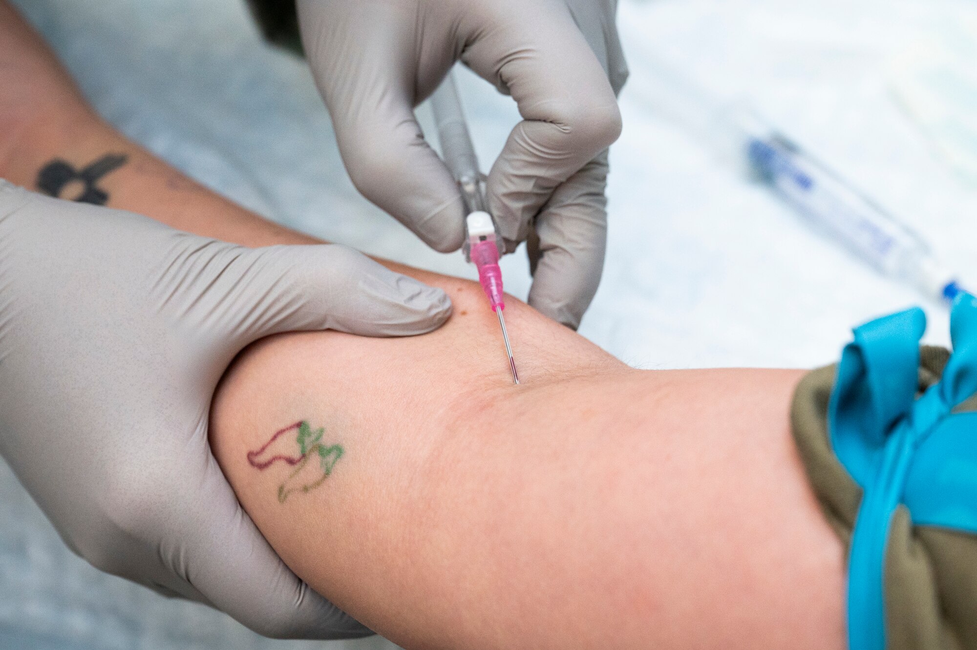 A 5th Medical Group Airman sticks a needle into another Airman's arm for IV training.