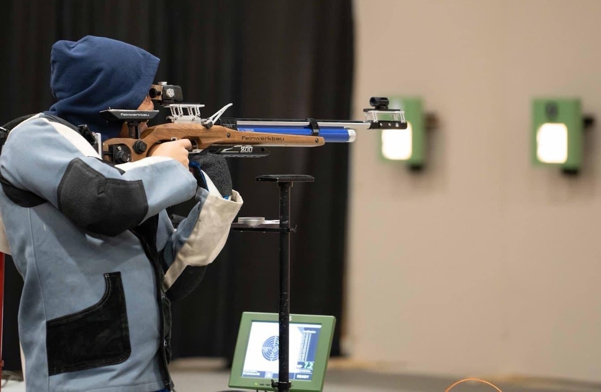side view of Lin taking aim at a target with an air rifle.
