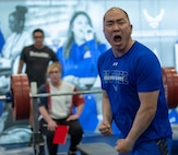 Lin shouts toward the camera with clenched fists with weightlifting equipment in the background.
