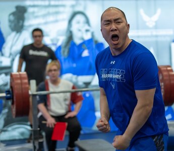 Lin shouts toward the camera with clenched fists with weightlifting equipment in the background.