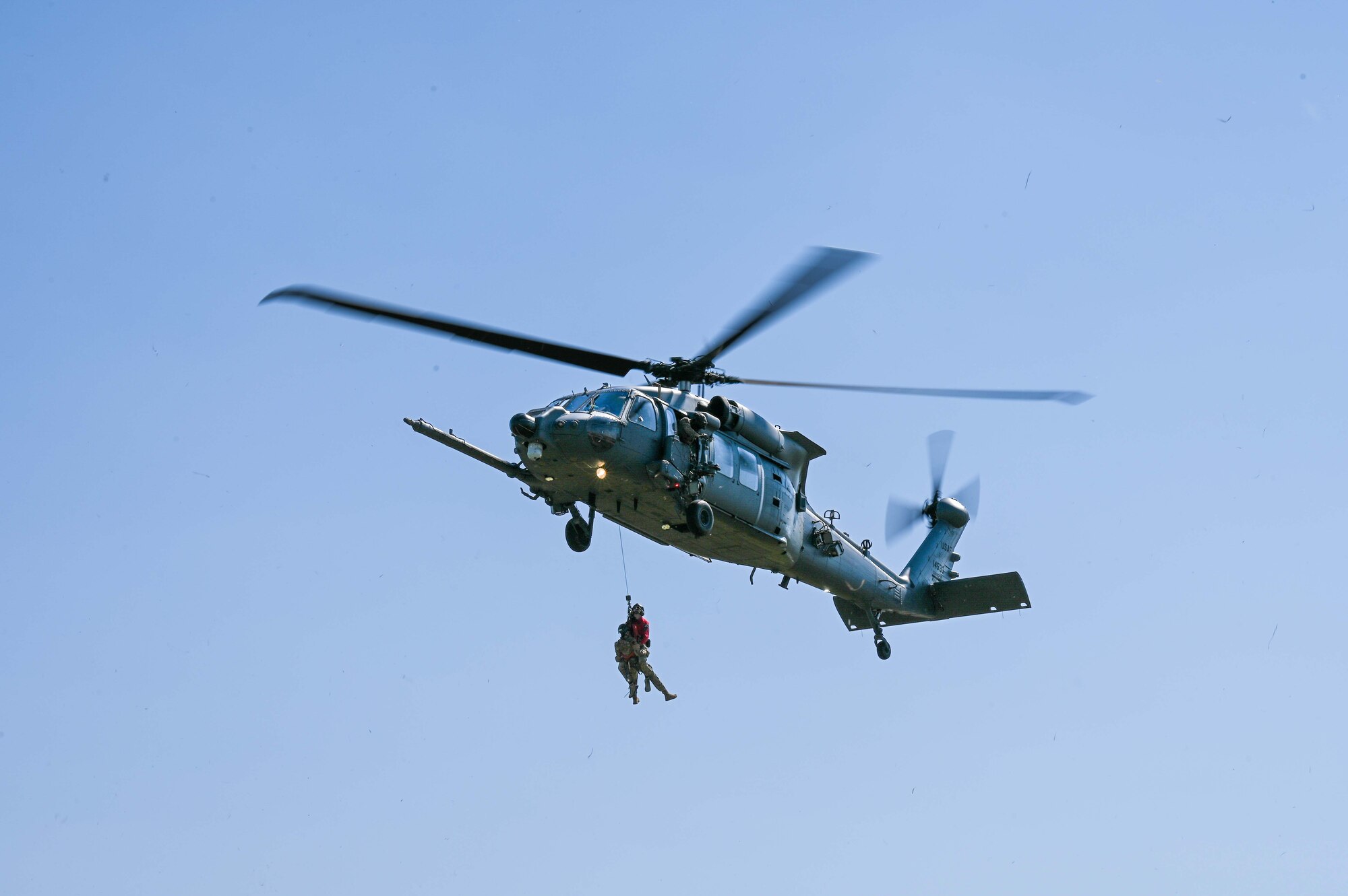Two service members are getting pulled into the helicopter.