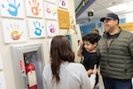 Five-year-old Nolan Rojas rings the bell at Walter Reed National Military Medical Center in Bethesda, Md., Feb. 28, to celebrate completing his leukemia treatment. His mother, Alex Rojas, stands beside him while his father, Ulysses Rojas, looks on proudly during the Ring of Bell ceremony in the Pediatrics Hematology/Oncology Clinic. The wall behind them is adorned with colorful handprint artwork from other pediatric patients, symbolizing hope and resilience. (DOD photo by Ricardo J. Reyes)
