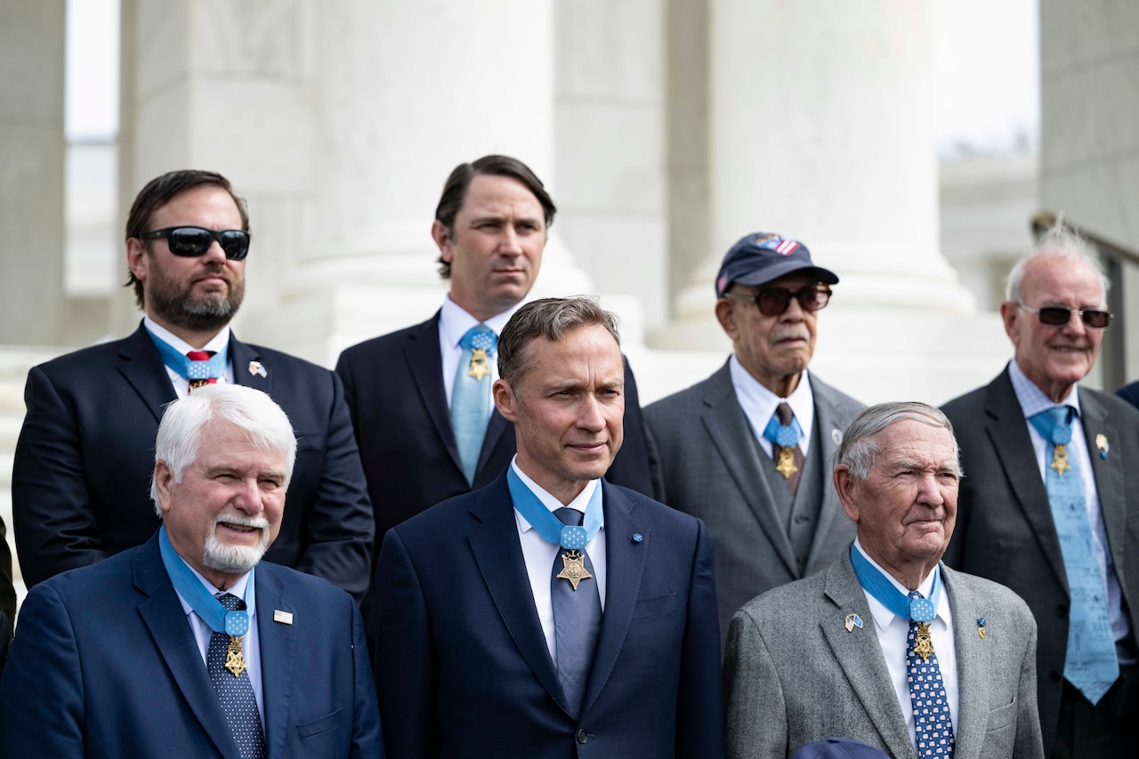 Medal of Honor recipients pose for a photo in front of marble columns.