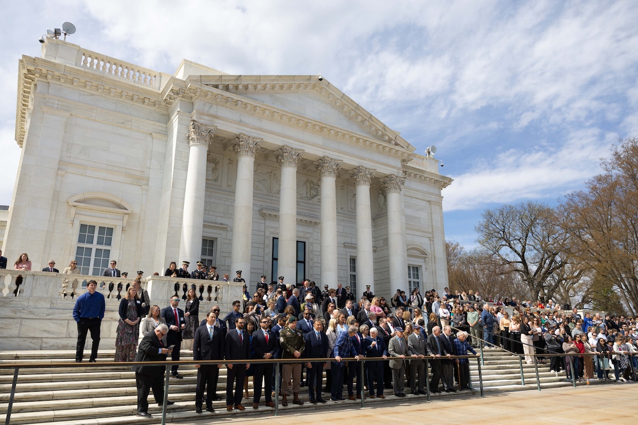 A group of veterans and people stand on steps in front of a white building with marble columns.