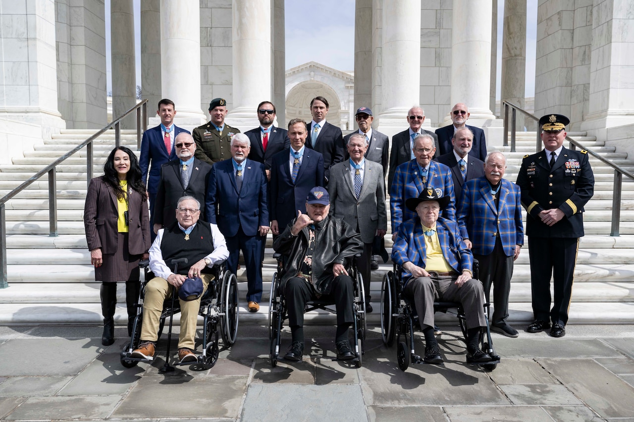 A group of veterans pose for a photo on white steps in front of marble columns.