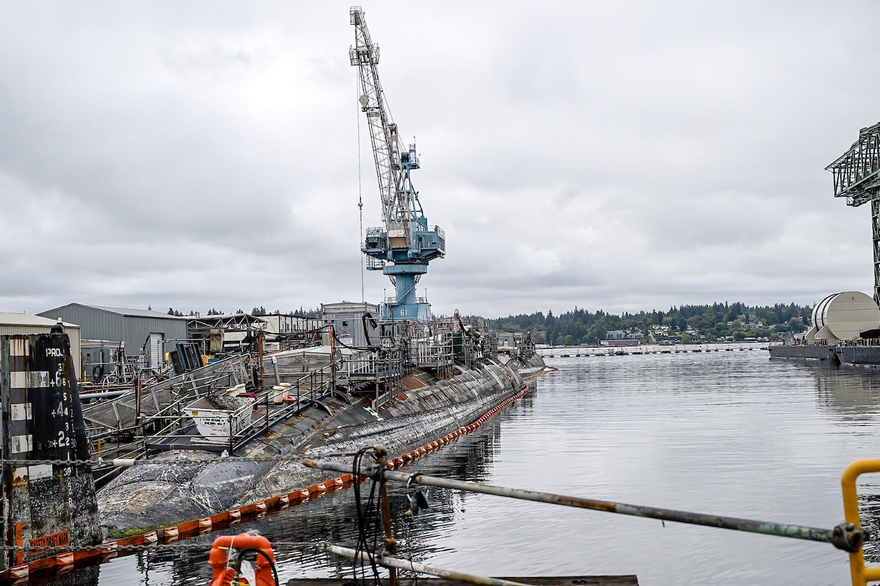 A crane on a pier sits beside a floating submarine.