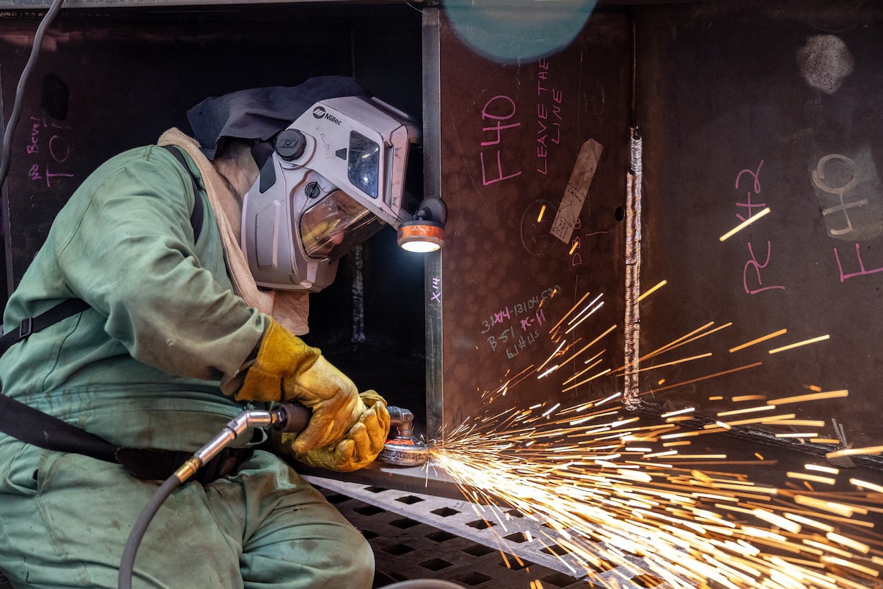 A weld gun shoots sparks as a person in protective gear and helmet pushes it around steel.