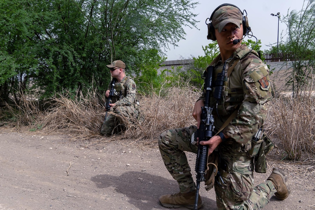 Two guardsmen kneel with weapons in the woods.