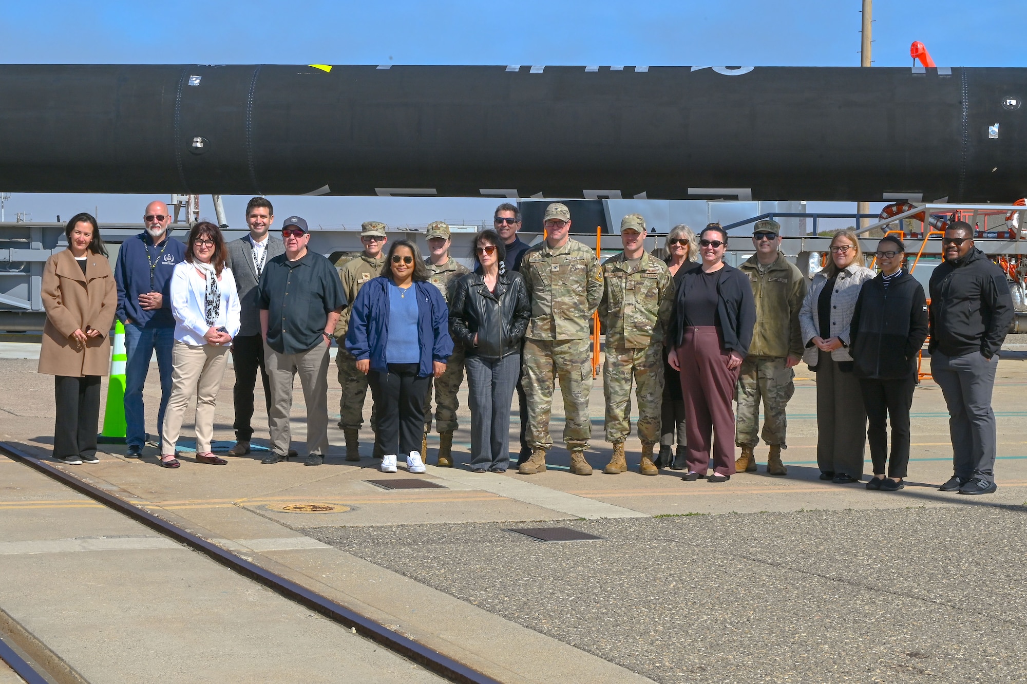 A group of people pose for a photo in front of a rocket oustide.