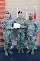 Three senior Army leaders stand together, the two on the left holding an award.