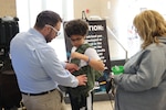 Josh Phillips, Naval Surface Warfare Center Indian Head Division’s public affairs officer, assists a student in securing a flight vest during the HITS Expo at Saint Charles High School in Waldorf, Maryland, March 22. (U.S. Navy photo by Staff Sgt. Arthur Jones/released)