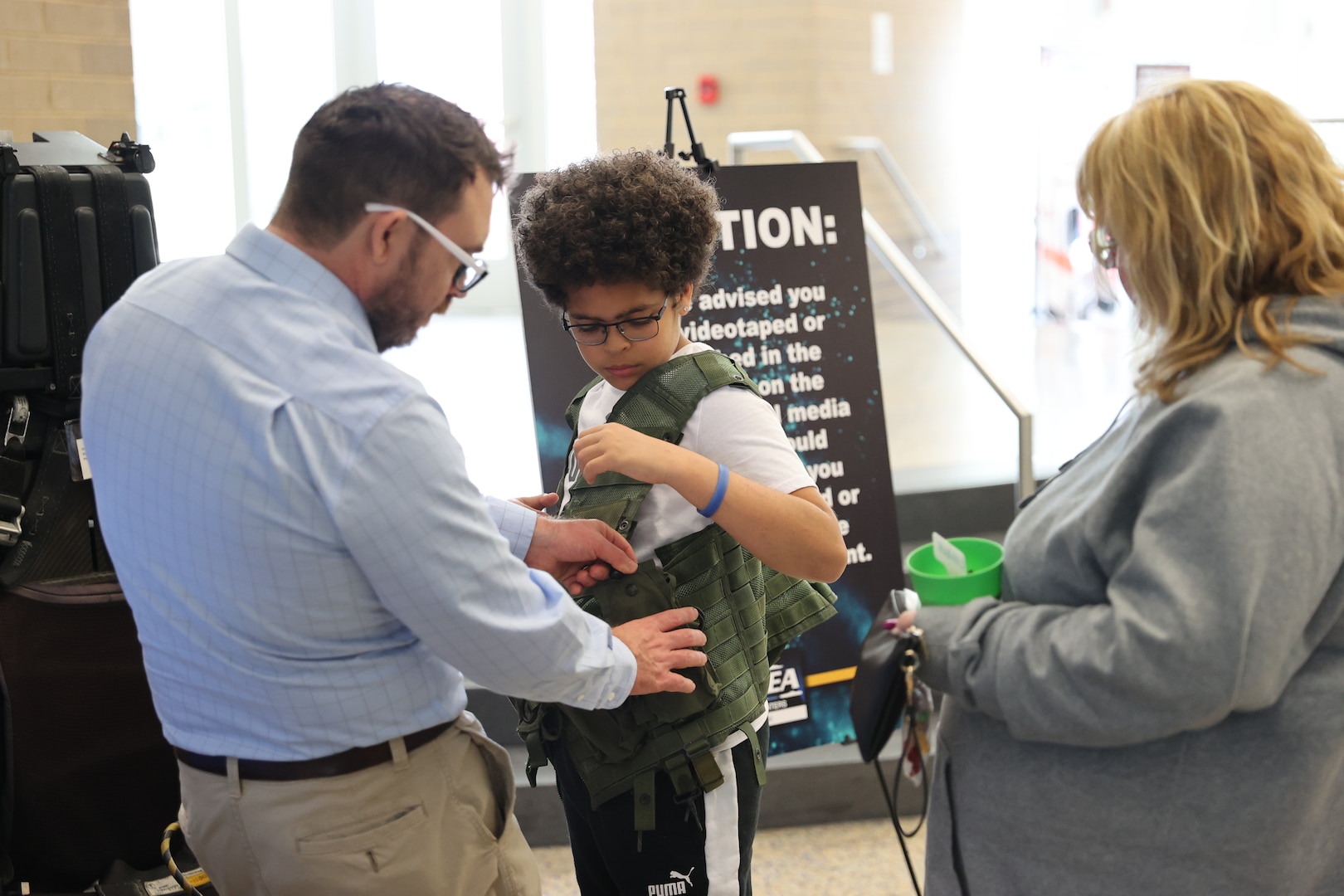 Josh Phillips, Naval Surface Warfare Center Indian Head Division’s public affairs officer, assists a student in securing a flight vest during the HITS Expo at Saint Charles High School in Waldorf, Maryland, March 22. (U.S. Navy photo by Staff Sgt. Arthur Jones/released)