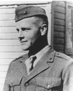 A man in an early 1940s-era military dress uniform is smiling while having his photo taken.