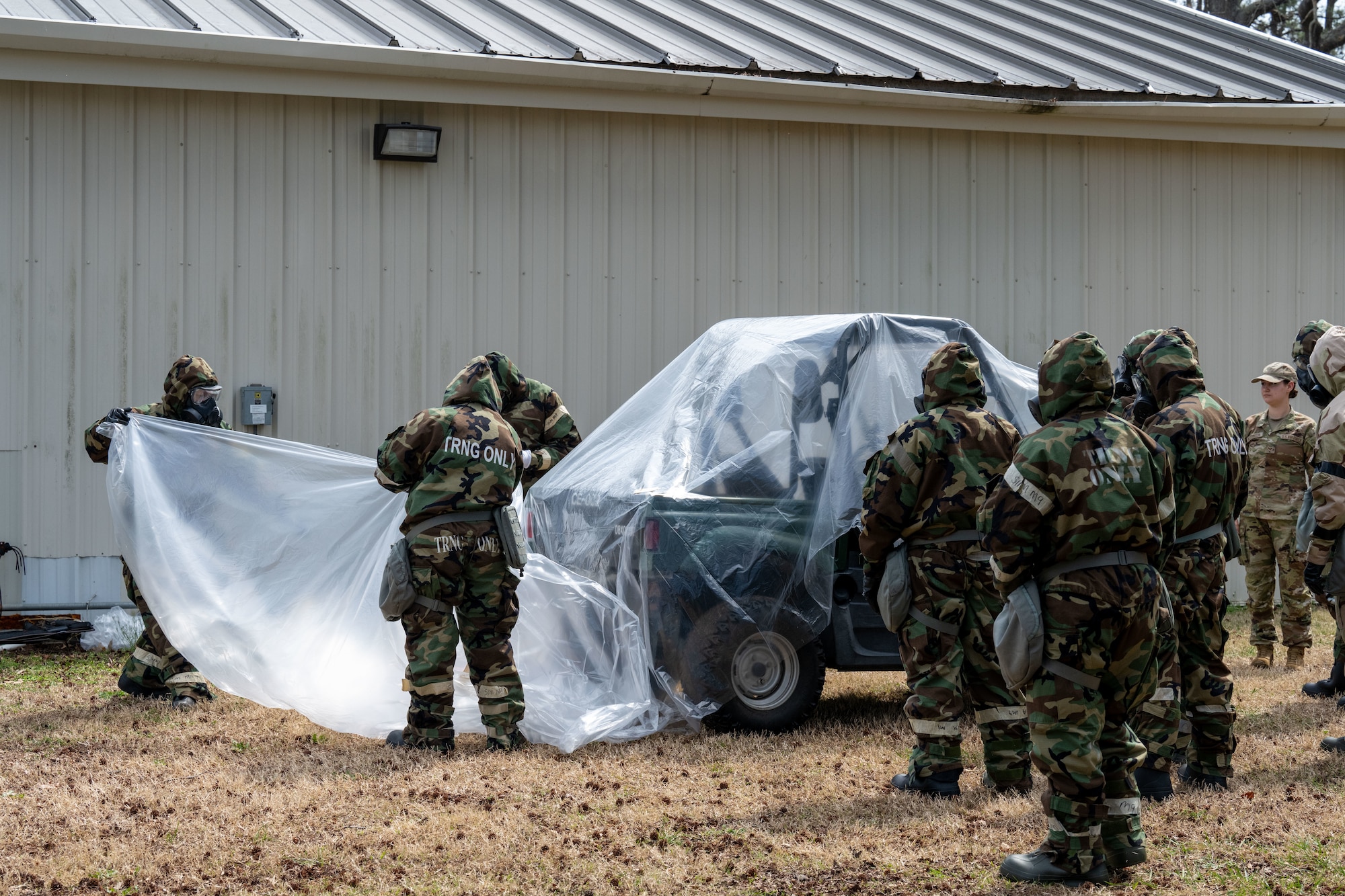 A group of uniformed members using clear plastic wrap to cover a small vehicle.