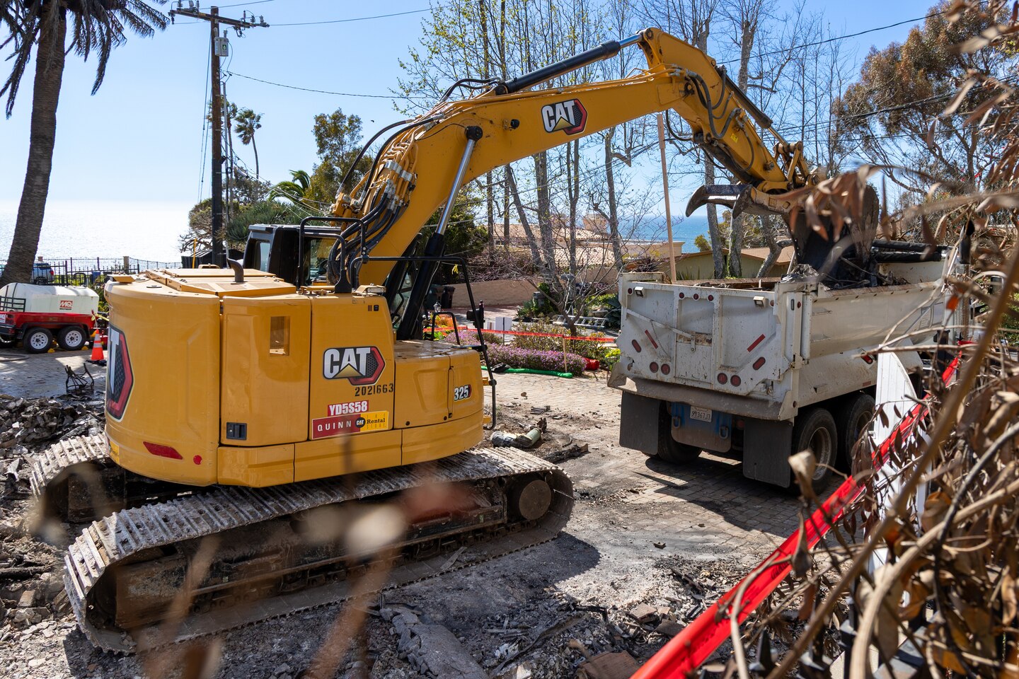 An excavator drops debris into a truck