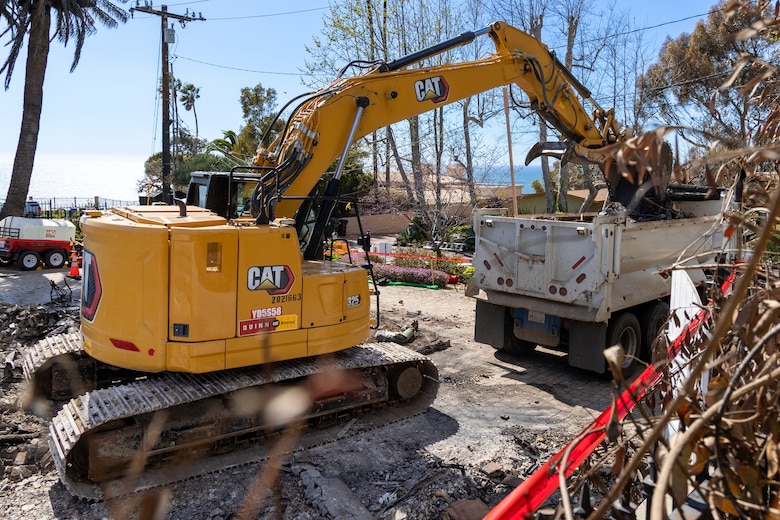 An excavator drops debris into a truck