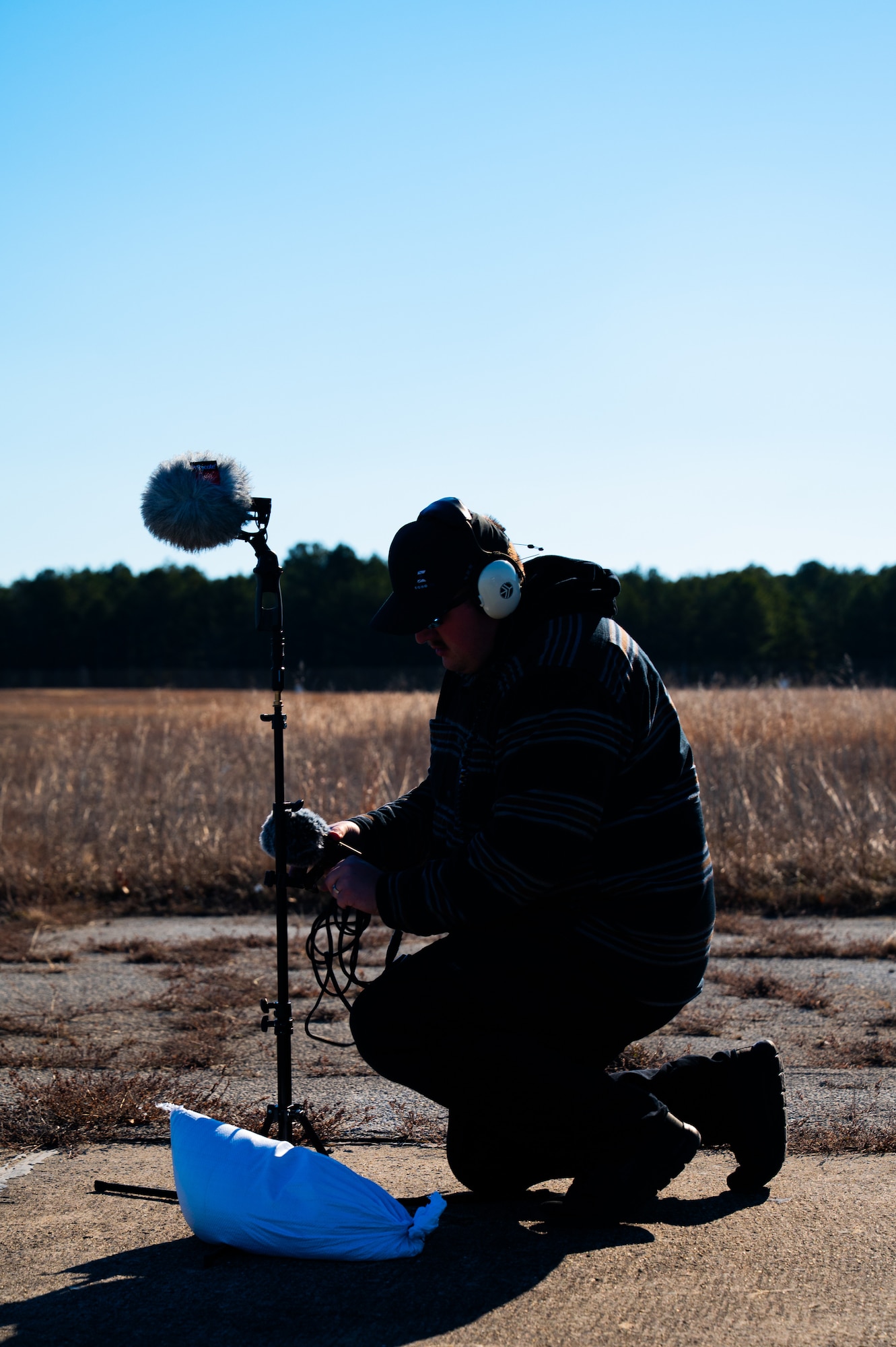 A man stands on a flightline while adjusting audio recording equipment.