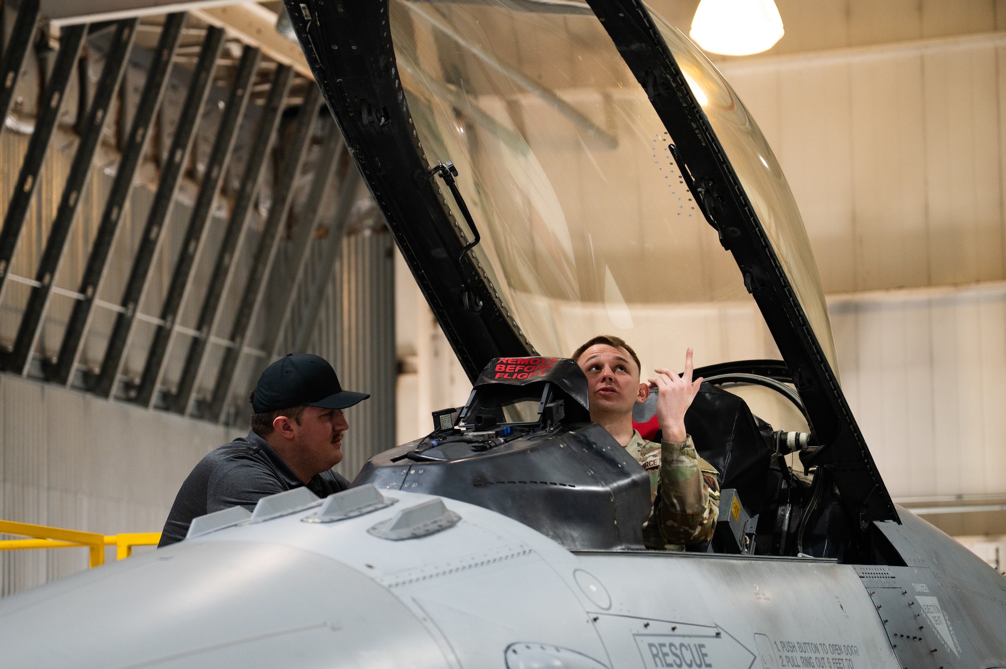 A man speaks to an Airman sitting in the cockpit of an F-16 fighter jet.