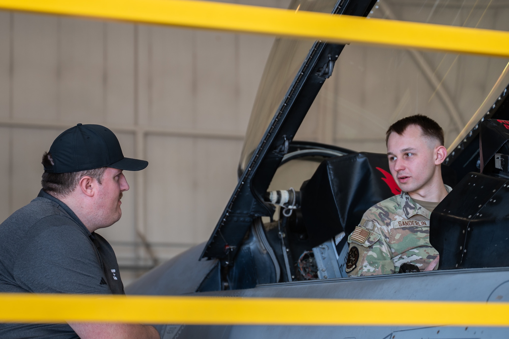 A man speaks to an Airman sitting in the cockpit of an F-16 fighter jet.