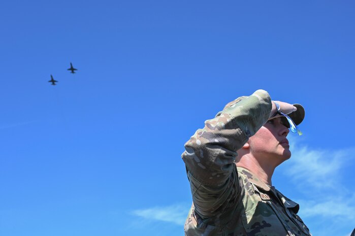 U.S. Air Force Chief Master Sgt. Jennifer Barger, 9th Reconnaissance Wing command chief, salutes the U.S. flag during the national anthem at the California Capital Airshow, as two T-38 Talon aircraft from Beale Air Force Base fly overhead, Mather, California, March 23, 2025.
