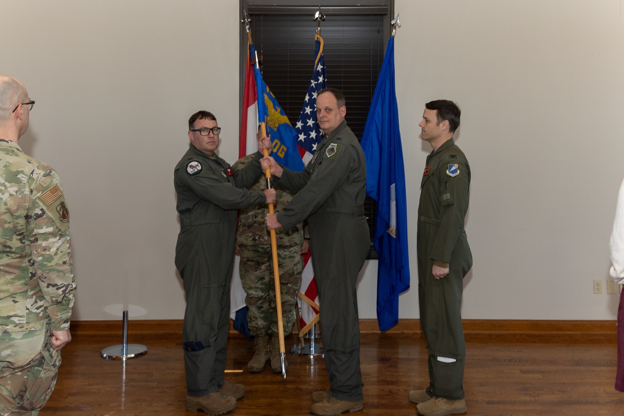 Two Air National Guard Airmen exchange a guidon flag during an official ceremony. The Airmen are wearing military flight suits.