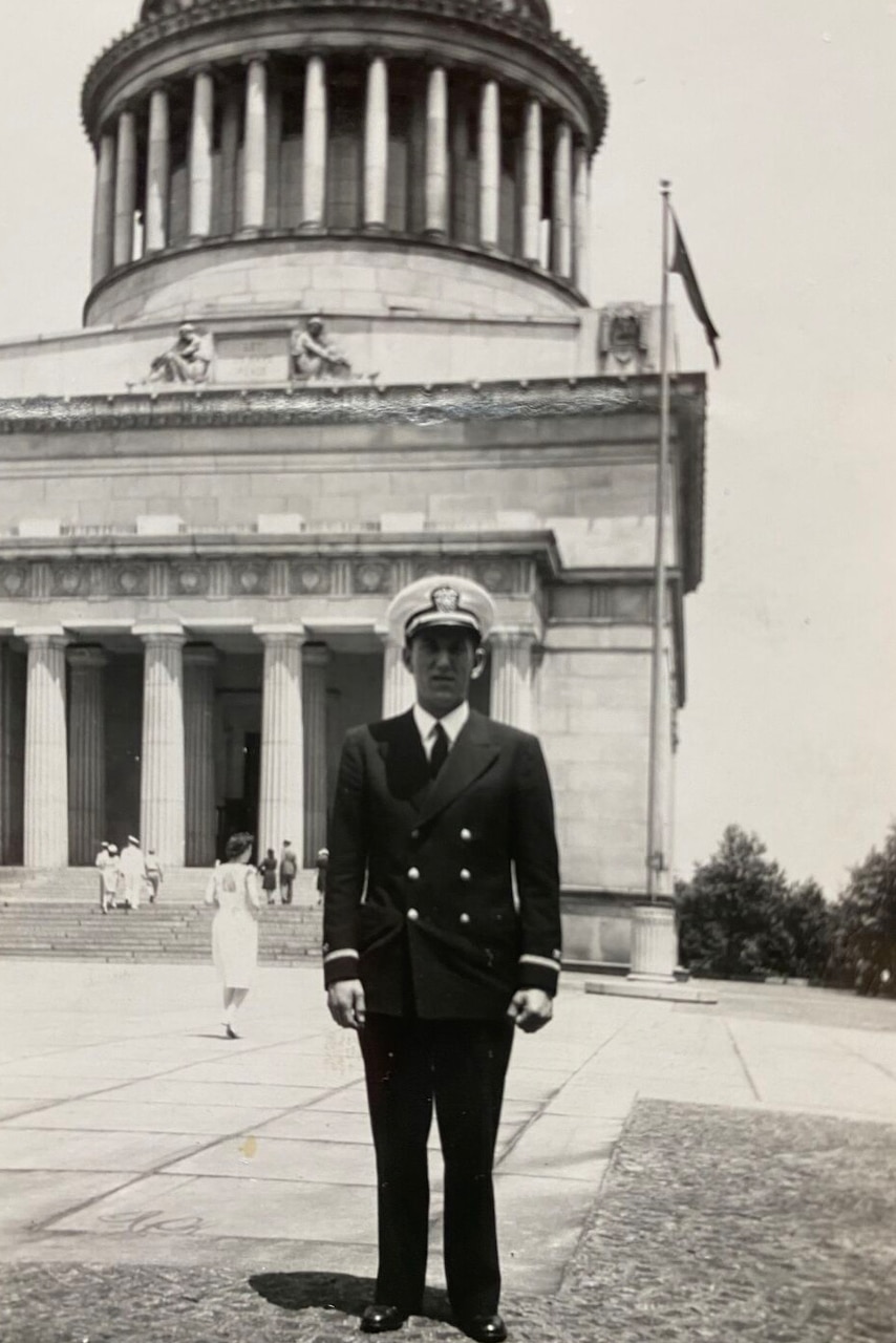 A man in a dress military uniform is standing at attention while having his photo taken.