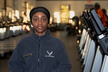 African- American female wearing a blue sweater with the white Air Force logo standing in front of a row of treadmills for a portrait shot.
